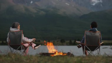Birkaç turist akşam ateşin başında oturur, ısınır ve dağ zirvelerini seyrederler. Turistler kamp kurdular. Aile turizmi.