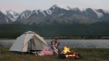 Birkaç turist akşam dağlarda çadırlı bir ateşin yanında oturur, ısınır ve ateşe bakarlar. Turistler kamp kurdular. Aile turizmi. Kamp..
