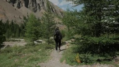 Sırtında sırt çantası olan bir turist dağ yolunda yürüyor. Dağlarda erkek turist. Dağlarda turizm.