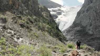 Sırtında sırt çantası olan bir turist buzulun dağ yolunda yürüyor. Dağlarda erkek turist. Dağ buzulu. Dağlarda turizm.