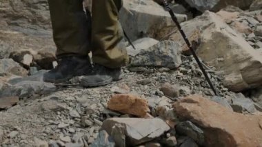 Yürüyüşçülerin bacaklarının yürüyüş direğiyle yakın çekimi. Yürüyüş direkleri olan bir turist kayaların üzerinden dağlara doğru yürür. Dağ turizmi.