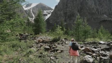 Sırtında sırt çantası olan bir turist dağ yolunda yürüyor. Dağlarda bir kadın turist. Dağlarda turizm.