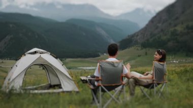 İki turist, bir kadın ve bir adam, dağlarda bir çadır kurdular. Turistler turist sandalyelerinde oturur ve yüksek dağların manzarasının tadını çıkarırlar. Dağlarda kamp yapmak..