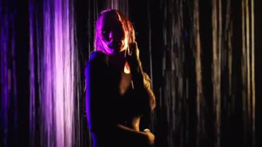 Karanlık bir stüdyoda, neon ışıkta düşen suyun arka planına karşı güzel bir kız. Neon ışıklı bir kızın portresi. Renkli ışık saçan bir kızın moda fotoğrafı..
