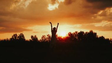 Gün batımında tarlada genç bir kızın silueti. Kız gün batımında kollarını kaldırır ve döner. Bir kız yazın sevinir, bir kızın silueti.