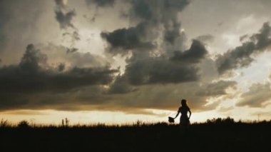 Tarlada koşan ve şapkasını fırlatan bir kızın silueti. Gün batımında elinde şapkasıyla genç bir kızın silueti. Koşan bir kızın silueti.