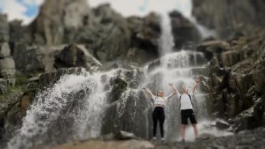 Birkaç turist bir dağ şelalesine tırmandı. Turistler ellerini kaldırır ve başarılarına sevinirler. Dağlarda aile turizmi.