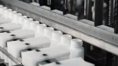 Kozmetik üretim tesisi. Beyaz şişeler bir taşıyıcı boyunca hareket eder ve ürünlerle doludur. Şampuan, duş jeli ve sıvı sabunla otomatik doldurma.