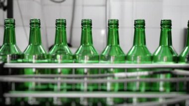 Bir fabrikada içki şişelemek için teknolojik bir yöntem. Boş yeşil cam şişeler taşıyıcı bant boyunca hareket eder. Fabrikada içki, alkol, limonata ve su için sıra var. İçecek üretim tesisi.
