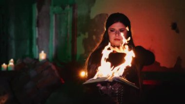 Elinde yanan bir kitapla cadı kostümü giymiş bir kız. Cadı elini yanan bir büyü kitabının alevinin üzerinden geçirir. Korku ve Cadılar Bayramı konsepti.