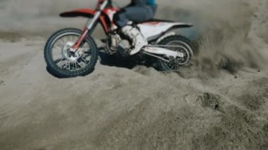 Tecrübeli bir motokros yarışçısı kumda, yakından dolaşır. Kum motosiklet tekerinin altından kameraya doğru uçuyor..