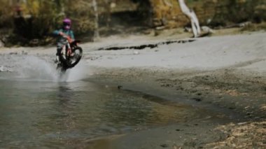 Dağ nehri boyunca motosiklet süren bir enduro binicisi. Su motosiklet tekerleklerinden farklı yönlere sıçrıyor. Dağ nehri boyunca motosiklet sürmek.