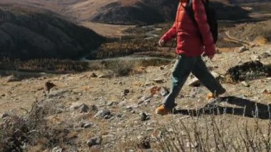 Omuzlarında sırt çantası olan kırmızı ceketli bir turist kız dağlarda yürüyor. Sonbaharda, bir turist dağlarda seyahat eder. Seyahat ve turizm kavramı.