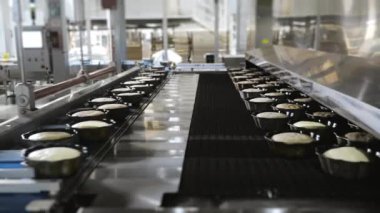 Kek kutularındaki hamurlar konveyör boyunca fırına gidiyor. Modern bir şekerleme fabrikasında kapkek üretimi. Otomatik kek üretimi.