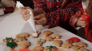 Erkek kardeşiyle birlikte küçük bir kız zencefilli çörekleri renkli jölelerle süslüyor. Yılbaşı tatilinde evde zencefilli kurabiye. Aile Noel için zencefilli kurabiye hazırlıyor.. 