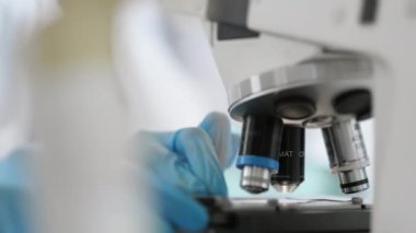 Bir tıp laboratuarı çalışanı bir bardağı mikroskop altına yerleştirir ve mikroskop lenslerini ayarlar. Modern bilim laboratuarı. Laboratuvar için araştırma ekipmanları.