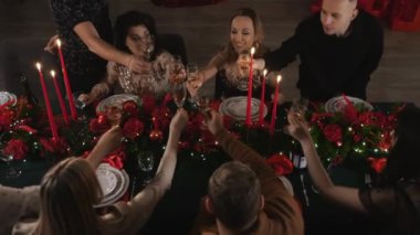Bir grup genç Noel 'i neşeyle kutluyor oturma odasında süslü bir masada oturuyor ve şampanya içiyor. Yeni yılı ve Noel 'i kutluyoruz.