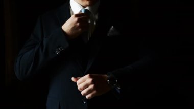 Kravatını düzelten takım elbiseli bir erkek işadamının yakın çekimi. Zarif giyimli bir adam kravatını düzeltir ve saatine bakar. Damat kravatını düzeltir..