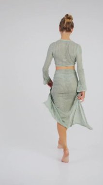 Yeşil mayo giyen ve kameraya pareo pozu veren güzel bir kız. Stüdyoda beyaz arka planda plaj kıyafeti giyen bir kız. Plaj modası. Mayolu kız. Dikey video.