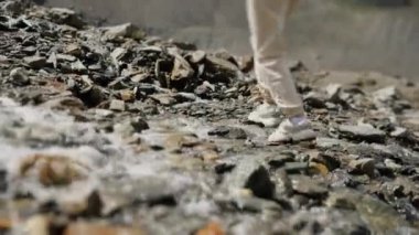 Dağlarda, dağ derelerinin arasında, taşların üzerinde yürüyen bir kızın yakın çekimi. Dağlardaki kız turist.