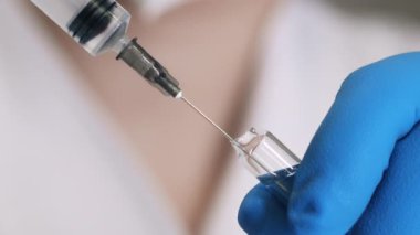 Mavi eldivenli bir doktorun, şırıngalı bir şişeden aşı çekerken yakın çekimi. Bir araştırmacı, şırıngayla şişeden bir madde çeker..