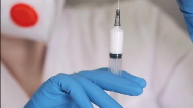 Mavi eldivenli ve solunum cihazlı bir doktor şırıngalı bir ampulden aşı çeker. Araştırmacı şırınga kullanarak şişedeki maddeyi alıyor..