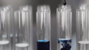 Pipetten dökülen mavi sıvı örneğinin laboratuardaki sıvı içeren test tüpüne yakın çekim. Sıvı örneğinin laboratuvar testleri. Virüsü inceliyorum. Laboratuvar testi.