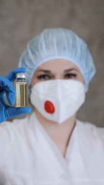 Solunum cihazlı ve koruyucu eldivenli bir doktor elinde aşı olan bir ampul tutuyor ve çerçeveye bakıyor. Doktor elinde ilaçla bir ampul tutuyor. Dikey video.