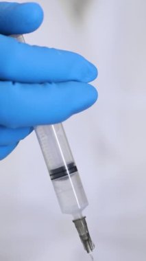 Aşıyla birlikte şırıngaya yakın çekim. Bir araştırmacı bir maddeye şırınga enjekte eder. Doktor hastaya bir iğne yapar. Dikey video.