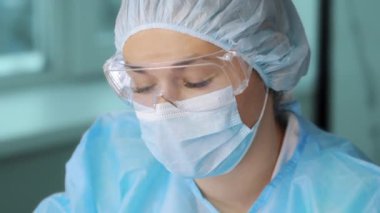 Kameraya bakan koruyucu maskeli ve güvenlik gözlüklü bir kadın doktorun portresi. Laboratuvarda bir bilim adamı kameraya bakar..