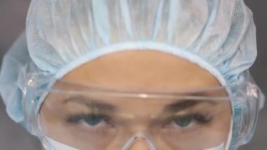 Koruyucu maske takan ve gözlük takan bir kadın doktor kameraya bakar. Laboratuvarda güvenlik gözlüğü takan bir bilim adamı kameraya bakar..