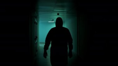 Koruyucu takım elbiseli iki doktor karanlık bir koridor boyunca bir hastanede yürüyor. Kimyasal koruyucu elbiseli iki kişi koridorda yürüyor..