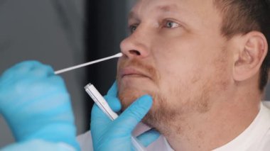Mavi koruyucu eldivenli bir tıp çalışanı, hastanın burnundan örnek alıyor. Virüsler için tıbbi test.