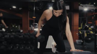 Spor salonunda dambılları kaldıran genç bir atletik kız antrenman yapıyor. Bir kız spor salonunda antrenman yapıyor. Dambıllı kol eğitimi.
