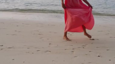 Pembe elbiseli genç bir kızın bacakları deniz kıyısında yalınayak yürüyor. Tropik bir adada kız turist. Bir kız sahilde yalınayak yürüyor..