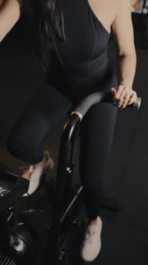 Spor salonunda egzersiz bisikletinde egzersiz yapan bir kızın ellerinin yakın çekimi. Egzersiz bisikletinde kardiyo çalışması. Kız spora gidiyor. Dikey video.