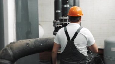 Güvenlik kaskı ve üniformalı bir mühendis hasar için bir fabrikada boru bağlantısını inceliyor. İş üniformalı bir mühendis. Bakım ve izleme.