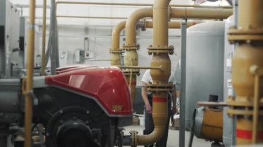 Kasklı ve üniformalı bir işçi elinde tabletle kazan dairesinde gaz boruları ve kazanlar boyunca yürüyor. İş üniformalı mühendis..