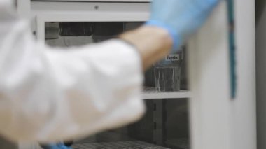 Tıbbi önlüklü ve koruyucu eldivenli bir bilim adamı buzdolabını açar ve donmuş örnekleri çıkarır. Modern ulusal laboratuvar. Buzdolabında DNA örnekleri var..