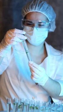 Laboratuvardaki bir kimyager bitki örneğiyle birlikte test tüpü alıyor. Alternatif bir biyolojik enerji kaynağının modern teknolojileri. Modern biyoloji laboratuvarı. Dikey video.