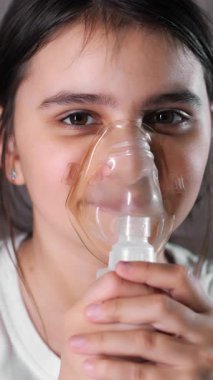 Nefes alan tıbbi maske takan küçük bir kız. Kız solunum yapıyor. Solunum hastalıklarının tedavisi için. Nefes alan tıbbi maske takan küçük bir kız. Dikey video.