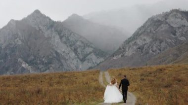 Düğün çifti gelin ve damat el ele tutuşun ve ileri doğru yürüyün. Dağlarda düğün. Dağlarda aşık bir çift, gelinlik giymiş..