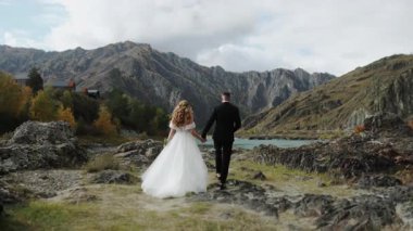 Düğün çifti gelin ve damat el ele tutuşun ve ileri doğru yürüyün. Dağlarda düğün. Dağlarda aşık bir çift, gelinlik giymiş..