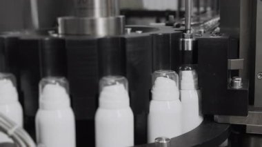 Otomatik sprey üretim hattı. Makine spreyle kapakları spreyin üzerine koyuyor. Beyaz sprey kutuları. Sprey üretebilir. Kozmetik fabrikası. Deodorant sprey üretimi.