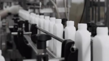 Kozmetik fabrikasında eldiven giyen bir işçi boş plastik şişeleri taşıyıcıya yerleştirir. Plastik şişe üretim tesisi. Beyaz boş plastik şişeler fabrikada bir taşıyıcı boyunca hareket eder..