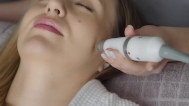 Eldivenli bir kozmetik uzmanı kozmetoloji kliniğinde genç bir kadının yüzünü vakumla temizliyor. Modern kozmetoloji kliniklerinde nemlendirici ve gençleştirici donanım prosedürleri.