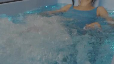 Mavi mayolu genç sarışın kadın küvette yatıyor ve hidroterapiden hoşlanıyor. Jakuzideki kadın. Spa merkezinde hidroterapi. SPA ve rahatlama.