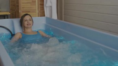 Mavi mayolu genç sarışın kadın küvette yatıyor ve hidroterapiden hoşlanıyor. Spa merkezinde hidroterapi. SPA ve rahatlama.