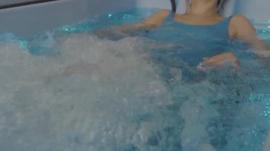 Mavi mayolu genç sarışın kadın küvette yatıyor ve hidroterapiden hoşlanıyor. Spa merkezinde hidroterapi. SPA ve rahatlama.