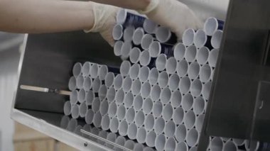 Fabrikada kozmetik ürünleri üretiliyor. Krem üretimi için taşıyıcı. Bir işçi doldurmak için plastik krem tüpleri konveyör bandına elle yerleştirir. Kremalı modern taşıyıcı. 